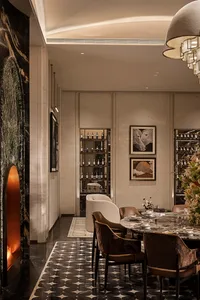 Elegant luxury dining room with dark marble fireplace, patterned black and white floor tiles, velvet dining chairs, built-in wine display, and contemporary artwork.