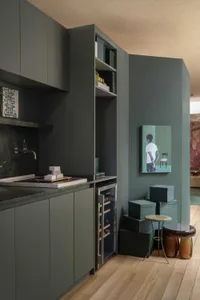 Modern sage green kitchen featuring matte cabinetry, black marble countertop, integrated wine cooler, open shelving, and contemporary wall art in a minimalist interior.