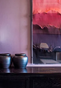 Two dark ceramic jars placed on a dark wooden console table beside a large abstract painting with red and purple tones.