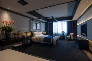 Modern luxury bedroom with black four-poster bed, dark wood furniture, white and navy bedding, and blue patterned carpet.