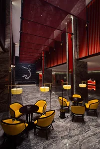 Luxurious hotel lobby featuring grey marble floors, yellow velvet armchairs, black tables, dramatic red ceiling panels, and a large white dragon mural on a black stone wall.