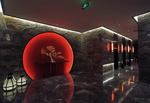 Modern luxury hotel lobby with dark marble walls, a large illuminated red circular feature wall containing a console table with bonsai tree, and geometric lanterns on the glossy floor.