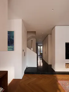 Modern minimalist interior hallway featuring herringbone pattern oak wood flooring, black slate tile entry, white textured walls, and a staircase with integrated storage.