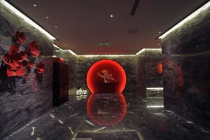 Luxurious modern Chinese-style lobby with dark marble walls and floor, featuring a glowing red circular moon gate with a bonsai tree inside, large red floral wall art, and black lacquered cabinet.