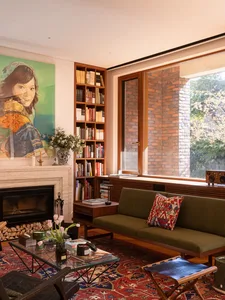 Cozy living room with olive green sofa, walnut bookshelf, brick wall, marble fireplace, and large colorful portrait painting