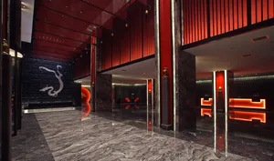 Luxurious hotel lobby featuring polished grey marble floors, dramatic red lacquered walls, a black stone dragon relief wall, and glowing red neon light installations.