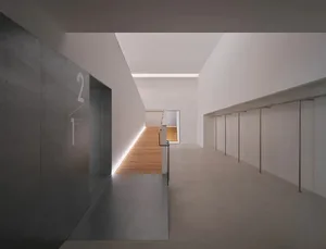 Modern minimalist interior hallway with grey concrete walls, light oak flooring, recessed LED lighting, and a view of a floating staircase in the distance.