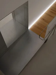 High-angle view of a modern minimalist staircase featuring grey polished concrete steps, a large concrete wall panel, light oak wood flooring, and a continuous linear LED light strip along the edge.