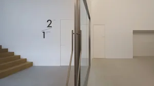 View looking up at a minimalist oak floating staircase with stainless steel handrail, white walls, and graphic 1/2 studio signage on the upper wall.