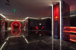 Luxurious hotel lobby featuring polished black marble floors, dramatic red circular wall features, dark textured paneling, and red accent lighting.