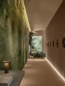 Modern interior hallway featuring a textured green wall, integrated greenery, circular wall art, and a distant reading nook with natural light.