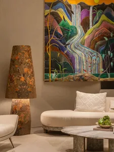 Modern living room featuring a large colorful abstract mountain and waterfall painting, a tall patterned floor lamp, cream curved sofa with white pillow, and marble coffee table.