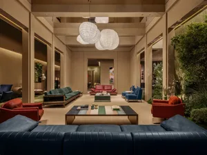 Modern luxury hotel lobby lounge with colorful sofas in red, teal, and navy, large spherical woven pendant lights, and integrated indoor greenery.