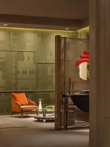 Modern living room featuring sage green patterned wall panels, burnt orange velvet armchair, round glass coffee table, and a bronze mesh room divider with red circular mirror.