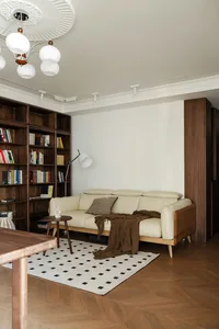 Modern living room with cream leather sofa, walnut bookshelf, black and white geometric rug, and white pendant light fixture.