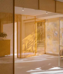 Modern commercial interior featuring golden perforated brass room dividers with dramatic light and shadow patterns on the floor.