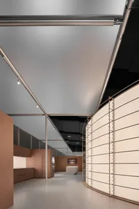 Modern exhibition hall interior featuring a prominent curved brushed stainless steel partition wall, light wood cabinetry on the left, and a long perspective view under a high ceiling with linear track lighting.