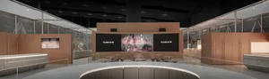 Modern luxury retail interior of Louis Vuitton store in Taipei with curved oak paneling, minimalist furniture, and large digital screens displaying brand imagery.