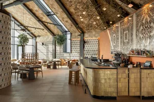 Modern restaurant interior with a curved terracotta-tiled bar, geometric brass pendant lights, patterned tile walls, wooden ceiling, and dining tables with neutral chairs.