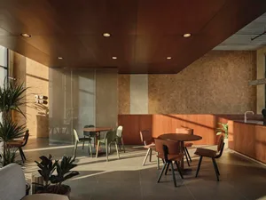 Modern cafe interior with round wooden tables, mixed green and brown leather chairs, wood-paneled walls and ceiling, and potted plants under natural sunlight.