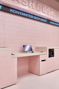 Modern cash desk covered in glossy pink square tiles with a built-in monitor and digital signage reading 'KONTANTER OCH KORT' against a matching pink tiled wall.