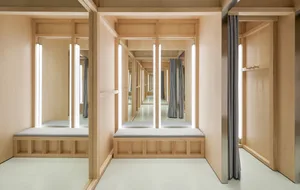 Modern Japanese style entryway with light wood cabinetry, grey upholstered built-in benches, vertical LED light bars, and multiple mirrors creating an infinite reflection hallway effect.