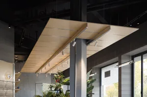 Modern industrial interior featuring a large suspended plywood ceiling canopy with integrated linear track lighting, concrete walls, and indoor plants.