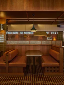 復古風格餐廳卡座，搭配棕色皮革座椅、深色木質壁板、圖案地毯與吊燈，營造溫暖復古氛圍。