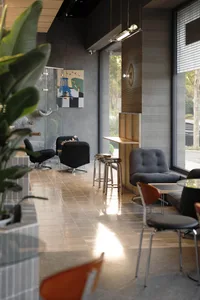 Modern cafe interior featuring ribbed wood paneling, black velvet swivel armchairs, grey corduroy lounge chair, metallic bar stools, and large windows with natural light.
