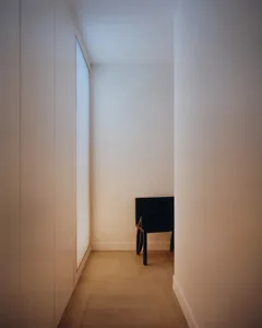 Narrow minimalist hallway with light oak herringbone floor, tall built-in cabinet on the left, and a black modern console table at the end under soft ambient lighting.