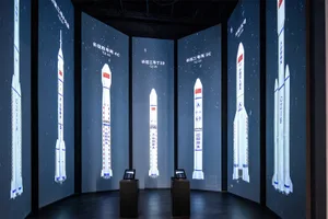 Dark exhibition room with curved walls covered in large LED screens displaying various Chinese Long March rockets against a starry background, with two interactive kiosks in the center.