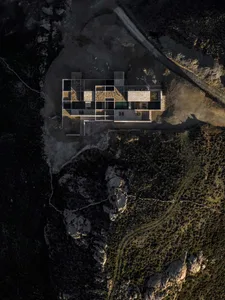 Aerial photograph of a modern stone villa with glass walls and an infinity pool built into a rocky mountain landscape at dusk.