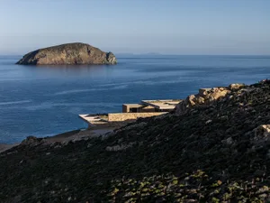 Modern stone and concrete cliffside villa overlooking the blue Mediterranean sea and a rocky island at golden hour.
