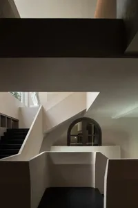 View of a modern sculptural concrete staircase with black steps, integrated shelving, and a dark arched doorway in the background.