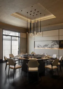 Elegant modern Chinese-style dining room featuring a large black marble round table, ten cream upholstered chairs, dramatic black pendant lights, and a backlit Chinese ink painting of pine trees and mountains.