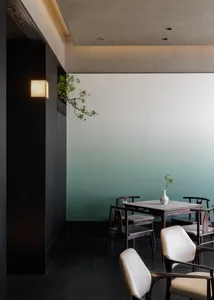 Modern dining area featuring a square walnut dining table, four dark wood armchairs with cream cushions, and a dramatic teal gradient accent wall with a bonsai tree.