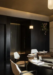 Modern luxury dining room featuring a large round dark wood table, white leather dining chairs, vertical LED wall lighting, and a hanging cherry blossom branch.
