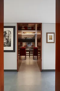 View through a doorway into a modern dining room featuring mirrored walls, red velvet dining chairs, dark wood accents, and contemporary art on white walls.