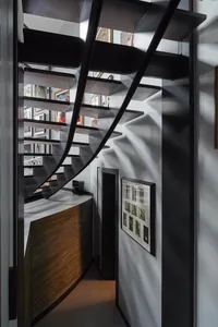 View of a modern black metal spiral staircase with wooden treads, a curved wood-paneled wall underneath, and a gallery wall of framed photographs on the right.