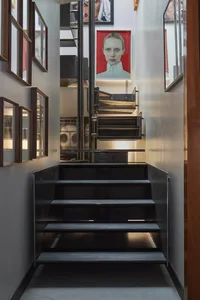 Modern black steel floating staircase with integrated lighting, flanked by dark wood framed portraits and a large red portrait of a woman at the top landing.