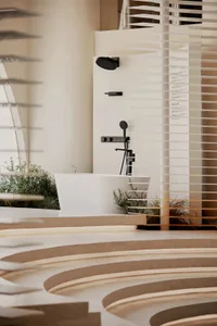 Modern minimalist bathroom with white freestanding bathtub, black matte fixtures, curved concrete steps, and horizontal wooden blinds allowing soft natural light.