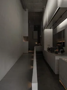 粗獷風商業廚房的狹長走廊，左側為原始混凝土牆面，右側為深色地磚與線性LED燈光，一人正在操作義式咖啡機。