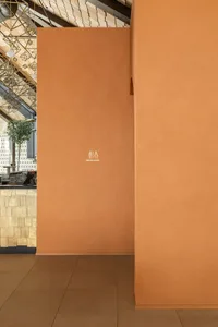 Orange terracotta plaster wall with white restroom signage in a modern cafe interior with wooden ceiling and tiled floor
