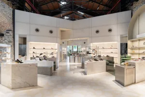 Modern minimalist shoe store interior with white marble display islands, integrated LED lighting, green velvet seating, and exposed industrial ceiling with skylights.