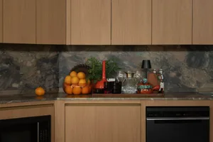 Modern kitchen counter with light oak cabinetry, dramatic multi-colored marble backsplash, and a variety of decorative objects including oranges, red vase, black lamp and ceramic pottery.