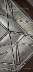 Low-angle architectural photograph looking up at a complex stainless steel space frame structure with concrete ceiling and translucent panels.