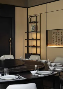 Modern Chinese-style dining room featuring a large round walnut table, white upholstered chairs, illuminated lattice wall panels, and a black metal display shelf with decorative ceramics and calligraphy art.