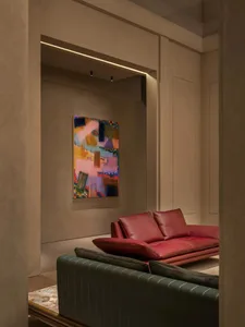 Modern living room corner featuring a red leather sofa, dark green striped armchair, and a large colorful abstract painting on a textured beige wall.
