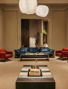 Modern luxury living room featuring a deep navy blue leather sofa, two vibrant red leather swivel armchairs, a low metallic coffee table, and a foreground striped leather ottoman with marble decor, all beneath large white woven spherical pendant lamps.