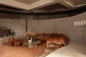 Modern living room featuring a large curved terracotta velvet sofa, marble coffee table, and curved wooden walls with warm earthy tones.